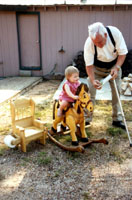 Her Great Papaw shows her a book while she rides the Pony built for her.